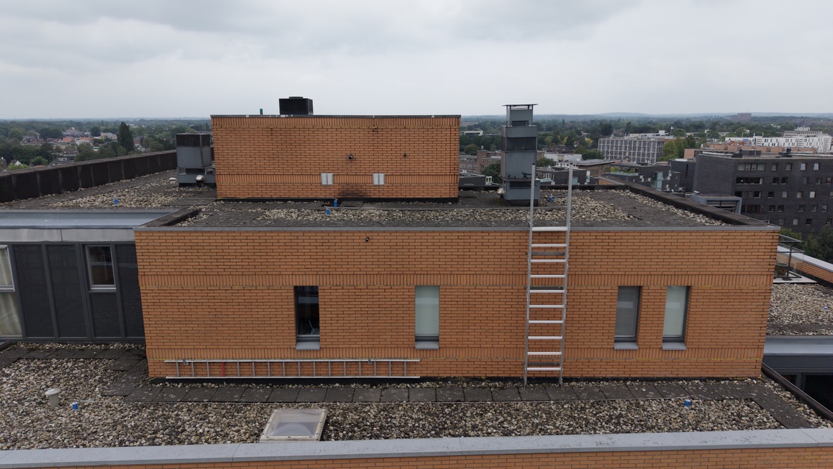 Detailopname op dakhoogte van metselwerk, dakbedekking, ventilatie en een vaste ladder